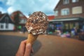 Close up of hand holding cone with white soft serve ice cream covered in chocolate sprinkles with blurry city scene Royalty Free Stock Photo