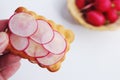 Hand holding crispbread with butter and sliced radish.