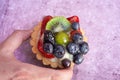 Close up of a hand holding a delicious fruit tart blueberries kiwi strawberries grapes and raspberries Royalty Free Stock Photo