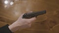 Close-up of hand holding gun at gunpoint. Stock. Dangerous criminal threatens with gun on background of wooden table