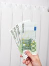 Close-up of a hand holding hundred euro banknotes. In the background, the central heating battery is white. The concept of high Royalty Free Stock Photo