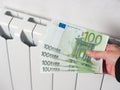 Close-up of a hand holding hundred euro banknotes. In the background, the central heating battery is white. The concept of high Royalty Free Stock Photo