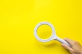 Close up hand holding magnifying glass on yellow background. SEO managment