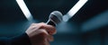 Close-up of a hand holding a microphone with blurred background and dramatic lighting in a dark environment Royalty Free Stock Photo