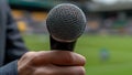 Close-up of a hand holding a microphone in front of a blurred stadium background Royalty Free Stock Photo