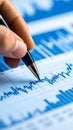 Close up of a hand holding a pen pointing at a financial graph with blue bars and line chart Royalty Free Stock Photo