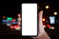 Close-up hand holding phone vertical, Using smart phone towards blurred traffic light at night background - copy space Royalty Free Stock Photo