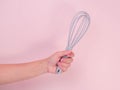 Close up of hand holding plastic whisk isolated on pink background. Kitchen tool for whipping cream or eggs Royalty Free Stock Photo
