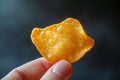 Close-up of a hand holding a single nacho chip, emphasizing its texture and the dark backdrop Royalty Free Stock Photo