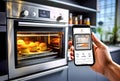 A close-up of a hand holding a smartphone, using an app to control a smart oven baking muffins in a minimalist kitchen. Reflects Royalty Free Stock Photo