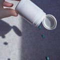 Close-up of hand holding white bottle with green pills falling on grey surface in soft light Royalty Free Stock Photo