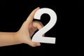 Close-up hand holding a white number 2 on a black background. Number two isolate on black background in child& x27;s hand Royalty Free Stock Photo
