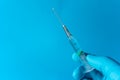 Close-up of a hand in the lower right corner of the image holding a syringe with a drop of liquid on the tip about to fall. All on Royalty Free Stock Photo