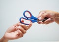Hand a male holding blue and red scissors give too hand a female on white background. Royalty Free Stock Photo