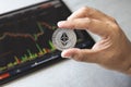 Close-up hand of man holding crypto coin on chart in tablet background. Blockchain technology finance future. Male hold Ethereum.