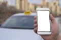 Close-up of a hand of a man holding a mobile phone in the background of a car and a city