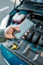 Close up of hand of man holding phone, calling emergency car service while standing near his broken car with open hood Royalty Free Stock Photo