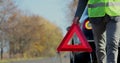 Close up hand of man putting warning triangle by the broken car on a road. Concept road accident. Help repair. Royalty Free Stock Photo