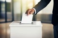 Close-up of a hand placing a vote into a white ballot box in a well-lit office environment