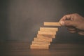 Close-up hand is placing wood block tower or jenga game stacked in stair step with caution to prevent collapse or crash Royalty Free Stock Photo