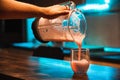 Close up of a hand pouring strawberry milkshake into a glass at a kitchen bar with orange ambient light and a blue teal light that