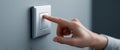 Close-up of a hand pressing a modern white light switch on a gray wall in a minimalistic interior setting with soft lighting Royalty Free Stock Photo
