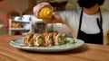 Close up of hand of professional sushi chef wearing protective mask and gloves decorating sushi rolls with falling Royalty Free Stock Photo