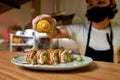 Close up of hand of professional sushi chef wearing protective mask and gloves decorating sushi rolls with falling Royalty Free Stock Photo