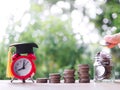 Close up hand putting coin into glass bottle, Red alarm with graduation hat and stack of coins. The concept of saving money for Royalty Free Stock Photo