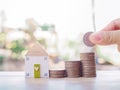 Close up hand putting coin in stack of coins with miniature house, The saving concept for house and property Royalty Free Stock Photo