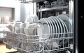 Close-up of a hand putting a dirty ceramic plate in the dishwasher. The concept of household and useful technology.