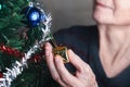 Close-up of hand senior woman decorating the Christmas tree while sitting in a living room at home. Space for text. Concept of Royalty Free Stock Photo