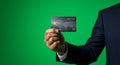 Close-up of a hand in a suit holding a modern, dark-colored credit card with technological design elements against a solid green Royalty Free Stock Photo