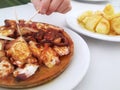 Close-up of a hand taking a piece of octopus from a portion of Galician octopus with potatoes