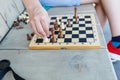 Close up hand of teenage plays chess on the bench. Boy makes a move with a wooden figure on a chessboard. Hobby, outdoor sport Royalty Free Stock Photo