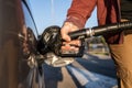 Close up on hand of unknown caucasian man hold black gas pump nozzle pouring gasoline into the fuel tank refueling petroleum to