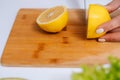 Close-up of hand of woman cutting fresh lemon using kitchen knife on board. Royalty Free Stock Photo