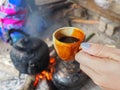 Close-up of hand woman holding a cup of coffee with old kettle on charcoal stove
