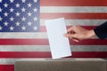 Close up of hand woman holding paper vote in the ballot box at on usa flag background