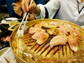 Close up hand of woman using chopsticks eating grill raw sliced beef and pork on the hot golden stainless steel stove Royalty Free Stock Photo