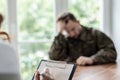 Close-up of a hand writing on a piece of paper with a depressed soldier in the blurred background