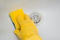 Close-up of a hand in a yellow rubber glove wipes a white sink with a sponge. Royalty Free Stock Photo