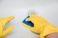 Close-up of a hand in a yellow rubber glove wipes a white sink with a sponge. Royalty Free Stock Photo