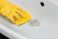 Close-up of a hand in a yellow rubber glove wipes a white sink with a sponge. Royalty Free Stock Photo