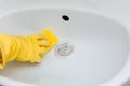 Close-up of a hand in a yellow rubber glove wipes a white sink with a sponge. Royalty Free Stock Photo