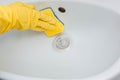 Close-up of a hand in a yellow rubber glove wipes a white sink with a sponge. Royalty Free Stock Photo