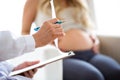 Hand of young doctor giving a routine check to beautiful pregnant woman and writing results. Royalty Free Stock Photo