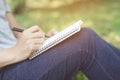 Close up hand young man are sitting on a marble chair. using pen writing Record Lecture note pad into the book in park public. Royalty Free Stock Photo