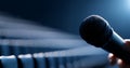 Close-up of a handheld microphone in a dimly lit empty auditorium with blurred rows of seats in the background Royalty Free Stock Photo