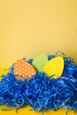 Close up Handmade paper easter eggs in blue paper nest on yellow backdrop